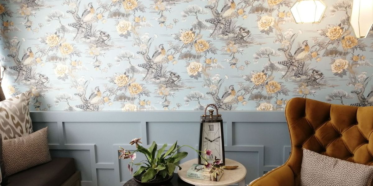 Sitting room with pale blue floral wallpaper above grey-blue panelled wainscoting, a mustard tufted armchair and small side tables