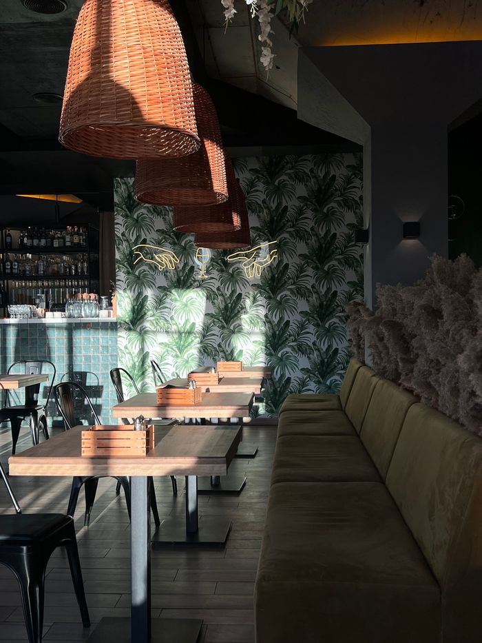 Empty restaurant dining room with woven pendant lamps and green palm-leaf wallcovering on the back wall