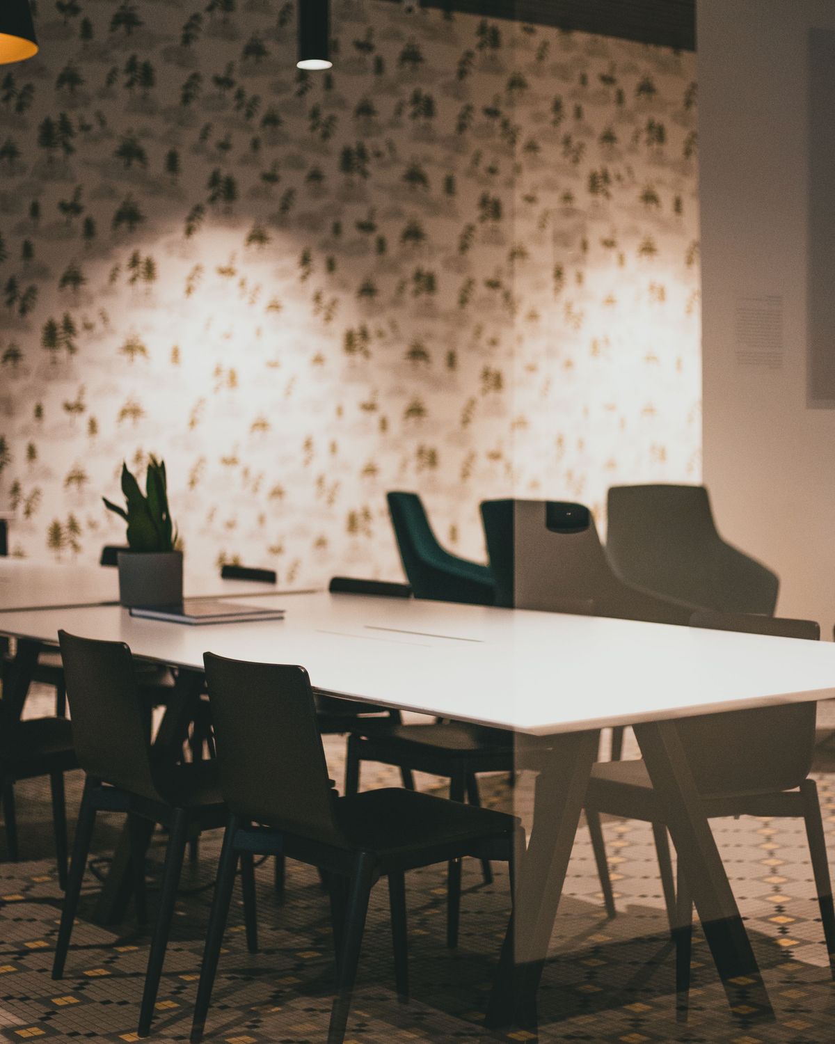 Meeting room with a long white table and black chairs in front of a softly lit patterned feature wall